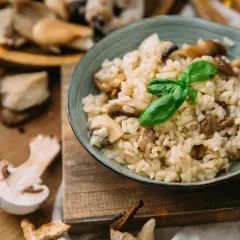 Aksamitny ryż do risotto z grzybami, udekorowany listkiem bazylii. Na drewnianej desce widać świeże grzyby i papryczkę chili.