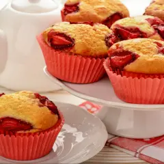 Pyszne muffiny z truskawkami w różowych papilotkach, gotowe do podania z białą czajniczkiem w tle.