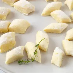 Kopytka z przepisu babci, delikatne i puszyste, posypane mąką, leżą na talerzu.