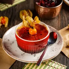 Słodka, karmelizowana crème brûlée w czerwonej kokilce, ozdobiona owocem miechunki.