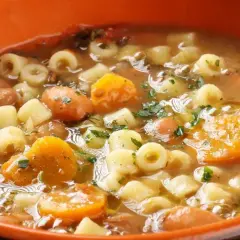 Gęsta zupa z makaronem, fasolą, marchewką i ziemniakami, posypana natką pietruszki. Idealna na chłodne dni.