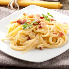 Pyszna carbonara z boczkiem, udekorowana natką pietruszki, na białym talerzu.