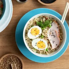 Miseczka z tantanmen, makaronem, jajkiem, mięsem i groszkiem. Obok sos sojowy i przyprawy.