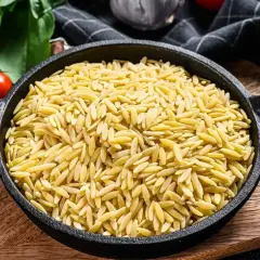 Czarny garnek pełen makaronu w kształcie ryżu, obok pomidory i zielenina.