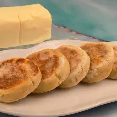 Pięć angielskich muffinek na talerzu, obok kostka masła. Idealne na śniadanie, jak u naszych moskali.