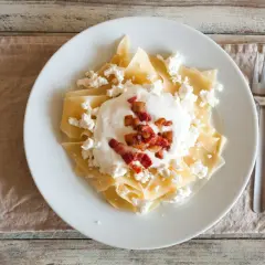 Makaron z twarogiem, śmietaną i skwarkami na białym talerzu.
