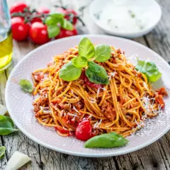 Talerz spaghetti bolognese z bazylią i parmezanem na drewnianym stole.