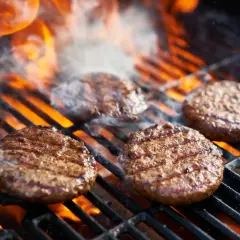 Aromatyczne burgery z grilla skwierczą na rozżarzonych węglach, otoczone dymem i płomieniami.