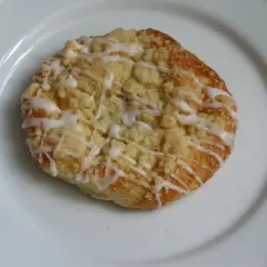 Szneka z glancem, puszyste ciasto drożdżowe z kruszonką i lukrem, na białym talerzu.