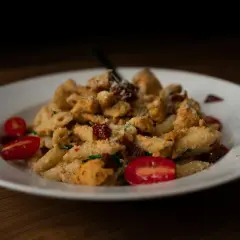 Penne z kurczakiem, suszonymi pomidorami i parmezanem, podane z pomidorkami koktajlowymi. Kremowy sos na bazie serka typu Philadelphia idealnie otula makaron.