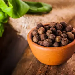 Garnek pełen aromatycznego ziela angielskiego na drewnianym blacie, obok zielone liście.