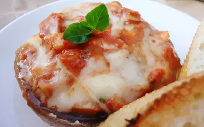 Pyszne pieczarki z grilla z ciągnącą się mozzarellą i sosem pomidorowym, udekorowane listkiem bazylii. Obok kromka chleba.