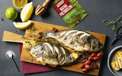 Dwie dorady z grilla, świeże cytryny, limonka i przyprawy tworzą apetyczną kompozycję.