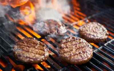 Aromatyczne burgery z grilla skwierczą na rozżarzonych węglach, otoczone dymem i płomieniami.