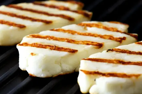 Trzy kawałki halloumi z grilla, z charakterystycznymi brązowymi paskami, leżą na czarnej, żebrowanej powierzchni.