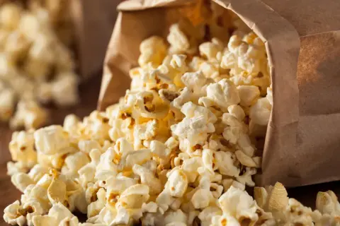 Góra popcornu wysypuje się z papierowej torby. Czy popcorn jest zdrowy? To zależy od sposobu przygotowania.