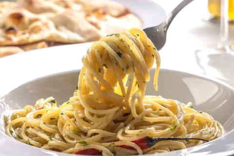Pyszne spaghetti na widelcu, idealne na trzy pomysły na szybki obiad z makaronem. W tle pieczywo.