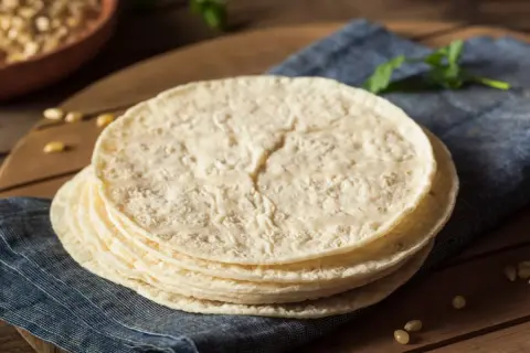 Stos świeżo upieczonych placków tortilla, które wyglądają jak z oryginalny przepis, leży na niebieskiej serwetce.