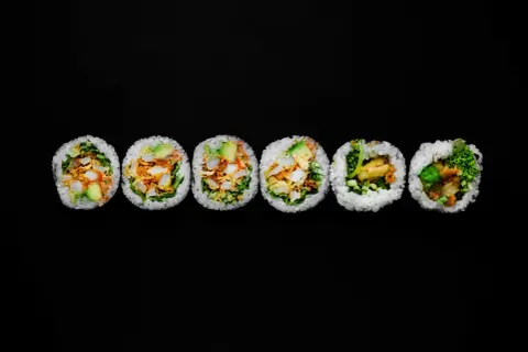 Sześć kawałków futomaki, czyli dużych rolek sushi, z awokado, warzywami i chrupiącym nadzieniem, ułożonych na czarnym tle.