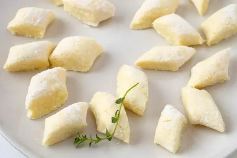 Kopytka z przepisu babci, delikatne i puszyste, posypane mąką, leżą na talerzu.