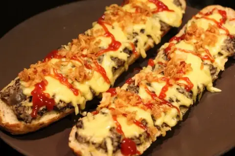Dwie zapiekanki z airfryer na bagietce, z serem, chrupiącą cebulką i ketchupem.