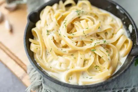 Kremowy makaron fettuccine w sosie śmietanowym, posypany natką pietruszki. Idealny pomysł, z czym zrobić makaron na szybko.