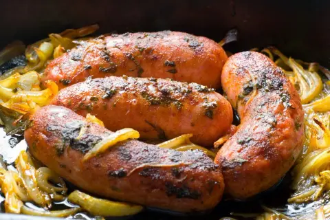 Soczysta kiełbasa z piekarnika jak z grilla, pieczona z cebulką i ziołami. Idealna na obiad!