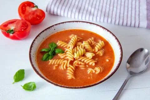 Aksamitna zupa pomidorowa z makaronem, ozdobiona bazylią. Idealne jakie przyprawy do zupy pomidorowej? Bazylia i czosnek!