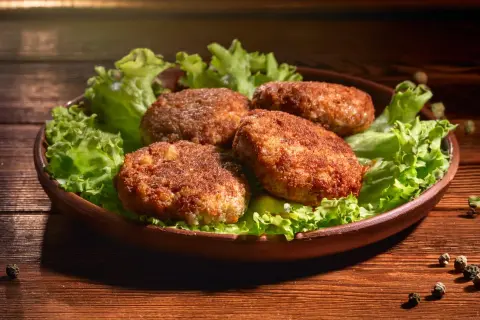 Cztery apetyczne kotlety mielone, idealnie wysmażone w airfryer, podane na liściach sałaty.