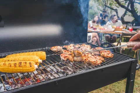Letnia biesiada z grillowaniem: soczyste kurczaki i kukurydza na ruszcie, w tle rodzina ciesząca się wspólnym posiłkiem.