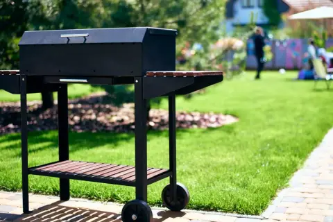 Czarny grill na kółkach w ogrodzie, gotowy na przyjęcie gości. Idealny pomysł na to, co na grilla tanio i smacznie.