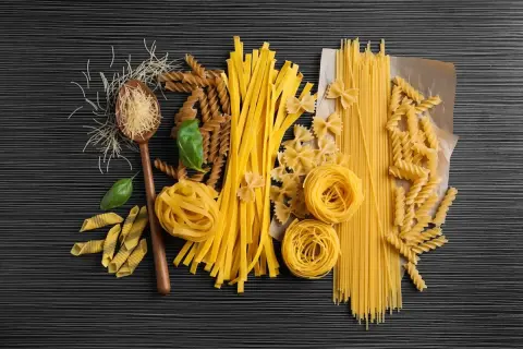 Różne rodzaje makaronu: spaghetti, fusilli, kokardki, tagliatelle, penne, nitki, na drewnianej łyżce.