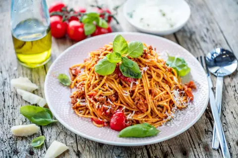 Talerz spaghetti bolognese z bazylią i parmezanem na drewnianym stole.