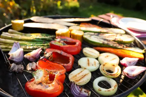 Pyszne warzywa na grilla: papryka, cukinia, szparagi, cebula i kukurydza pieczone na ruszcie w słoneczny dzień.