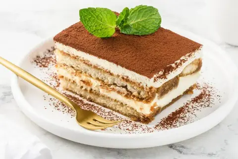 Pyszny kawałek tiramisu z mascarpone, posypany kakao i udekorowany miętą. Idealny sprawdzony przepis na deser.