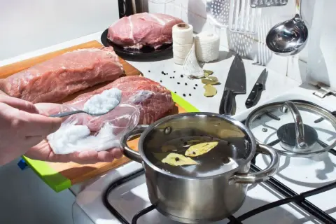 Przygotowanie solanki do mięsa. Na stole surowe mięso, przyprawy, sznurek i garnek z wodą.