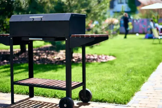 Czarny grill na kółkach w ogrodzie, gotowy na przyjęcie gości. Idealny pomysł na to, co na grilla tanio i smacznie.