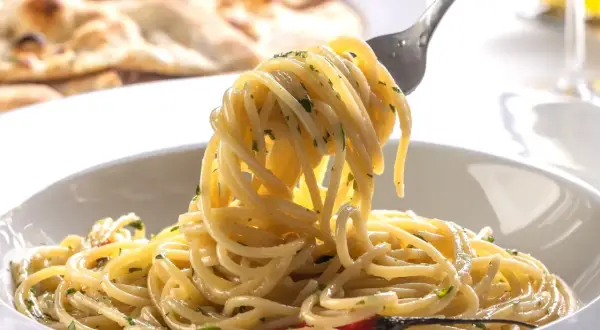 Pyszne spaghetti na widelcu, idealne na trzy pomysły na szybki obiad z makaronem. W tle pieczywo.