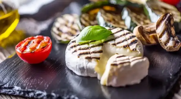 Ciepły camembert z grilla, z roztopionym wnętrzem, podany z grillowanymi warzywami i pomidorkiem.
