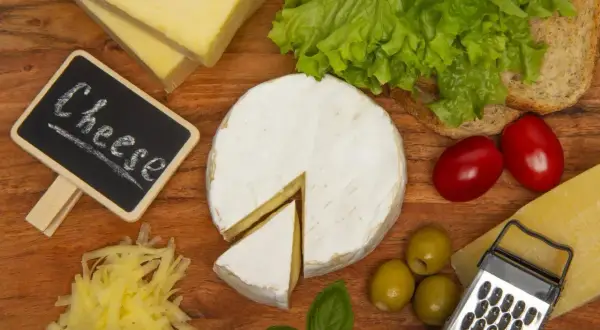 Deska serów: camembert, parmezan, żółty ser, oliwki, pomidorki, sałata i pieczywo. Ser corregio w centrum uwagi.