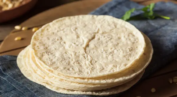 Stos świeżo upieczonych placków tortilla, które wyglądają jak z oryginalny przepis, leży na niebieskiej serwetce.