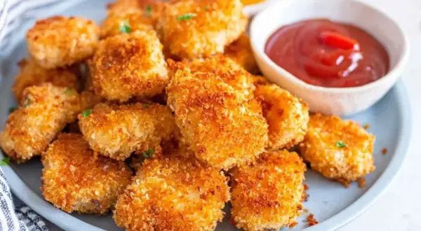 Chrupiące nuggetsy z airfryer na talerzu, obok miseczka z ketchupem. Idealna przekąska dla każdego.