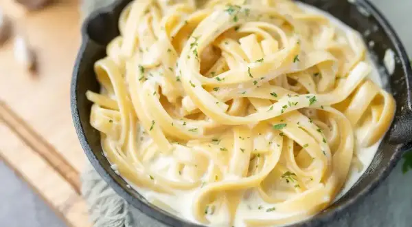 Kremowy makaron fettuccine w sosie śmietanowym, posypany natką pietruszki. Idealny pomysł, z czym zrobić makaron na szybko.