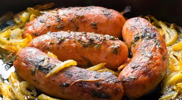 Soczysta kiełbasa z piekarnika jak z grilla, pieczona z cebulką i ziołami. Idealna na obiad!