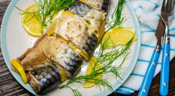 Pieczona makrela z cytryną i koperkiem na talerzu, gotowa do podania z niebieskimi sztućcami.