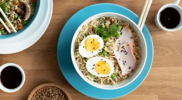 Miseczka z tantanmen, makaronem, jajkiem, mięsem i groszkiem. Obok sos sojowy i przyprawy.