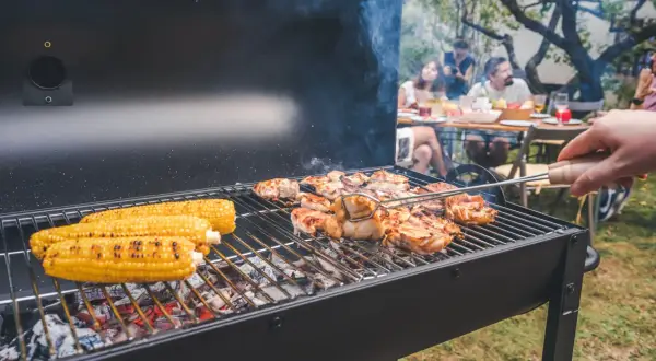 Letnia biesiada z grillowaniem: soczyste kurczaki i kukurydza na ruszcie, w tle rodzina ciesząca się wspólnym posiłkiem.