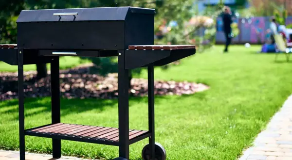 Czarny grill na kółkach w ogrodzie, gotowy na przyjęcie gości. Idealny pomysł na to, co na grilla tanio i smacznie.