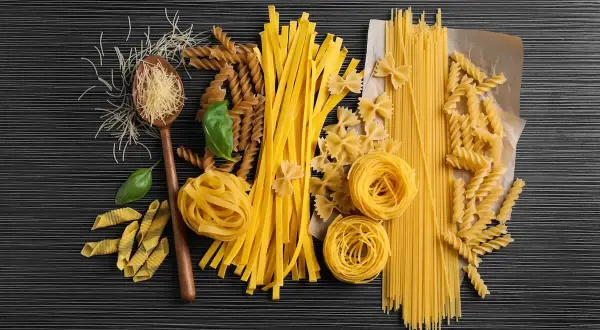 Różne rodzaje makaronu: spaghetti, fusilli, kokardki, tagliatelle, penne, nitki, na drewnianej łyżce.