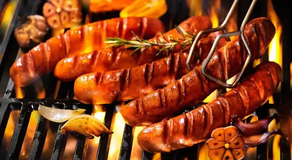 Aromatyczna kiełbasa z grilla skwierczy na ruszcie, otoczona płomieniami i przypieczonym czosnkiem.